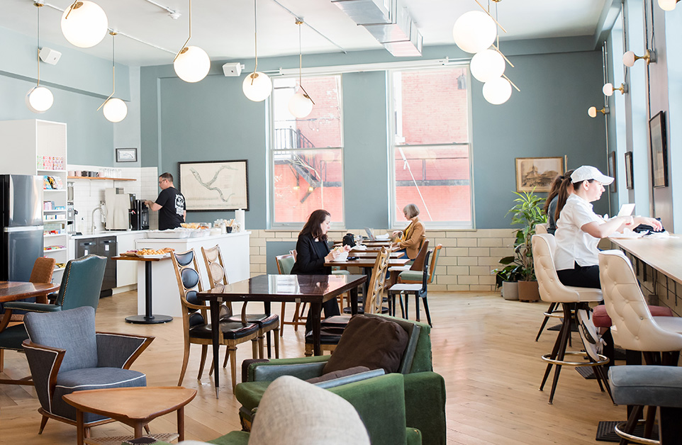 Open cafe and coworking floor with communal tables and lounge seating at Fulton Commons in Pittsburgh's Manchester neighborhood