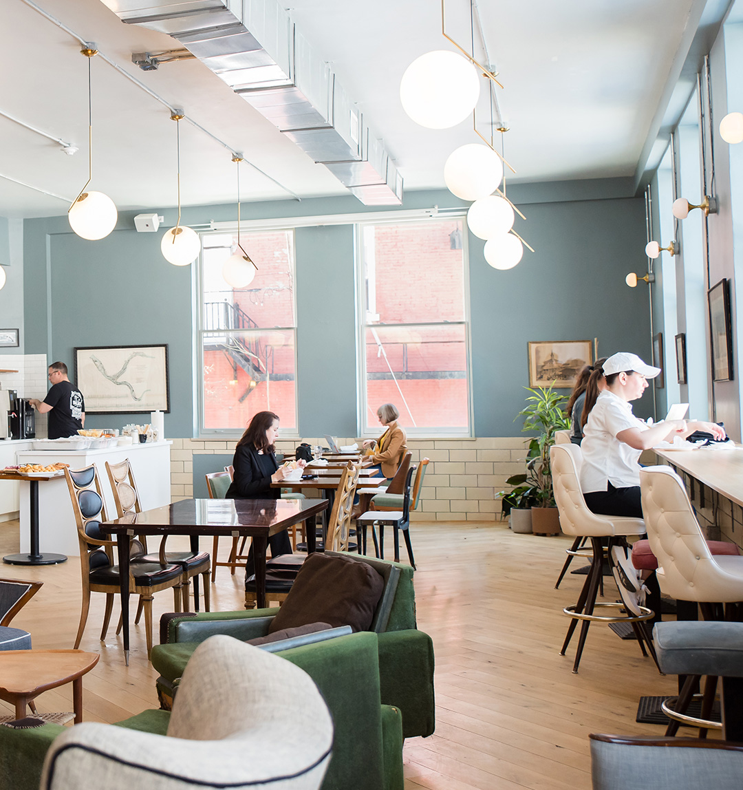 Open cafe and coworking floor with communal tables and lounge seating at Fulton Commons in Pittsburgh's Manchester neighborhood