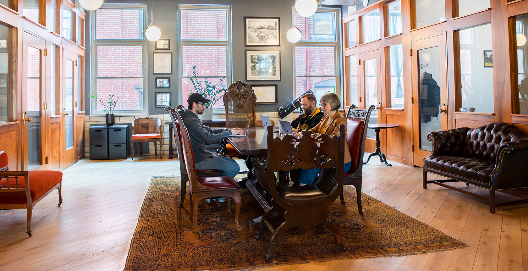 The Library Room at Fulton Commons coworking space Pittsburgh — antique table and leather seating with brick-view windows