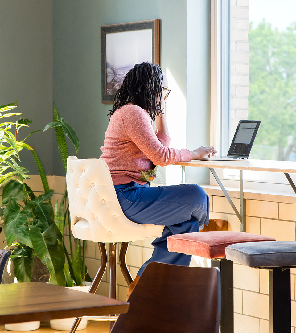 Coworking member working on a laptop at a sunlit window counter at Fulton Commons in Pittsburgh's Manchester neighborhood
